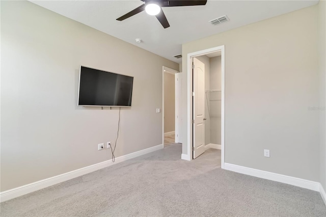 unfurnished bedroom with a walk in closet, carpet flooring, baseboards, visible vents, and a ceiling fan