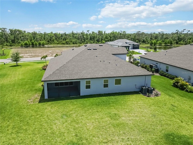 rear view of house with cooling unit, a water view, a shingled roof, stucco siding, and a lawn