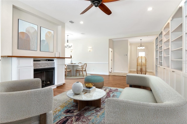 living area with light wood finished floors, visible vents, baseboards, a brick fireplace, and ceiling fan with notable chandelier