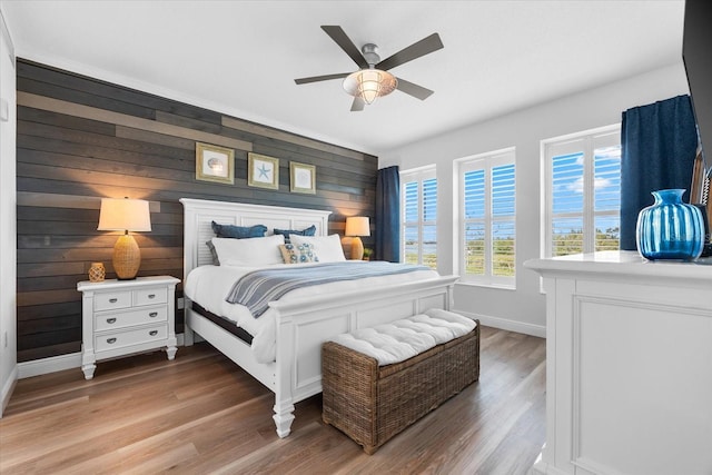 bedroom featuring wooden walls, wood finished floors, baseboards, and ceiling fan