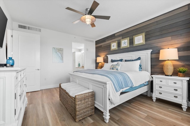 bedroom with visible vents, light wood-style flooring, wooden walls, a ceiling fan, and baseboards
