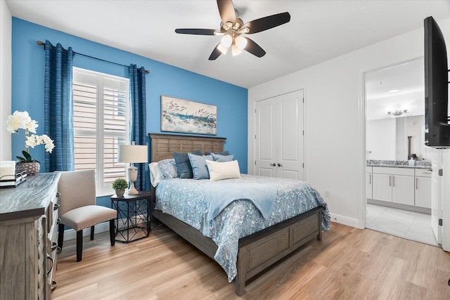 bedroom with a ceiling fan, a closet, baseboards, ensuite bath, and light wood-style floors