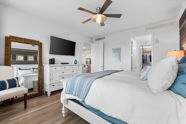 bedroom featuring light wood finished floors, a spacious closet, ceiling fan, and visible vents