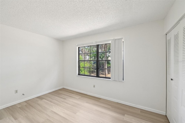 unfurnished bedroom featuring a closet, a textured ceiling, baseboards, and light wood-style floors