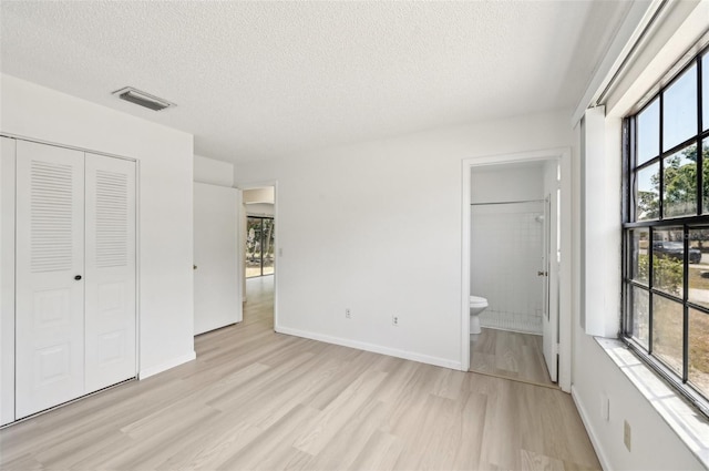 unfurnished bedroom featuring light wood-style floors, a closet, a textured ceiling, and visible vents