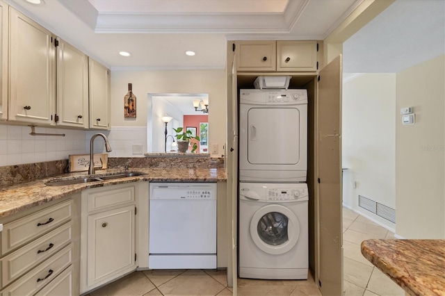 clothes washing area featuring laundry area, crown molding, light tile patterned flooring, stacked washing maching and dryer, and a sink