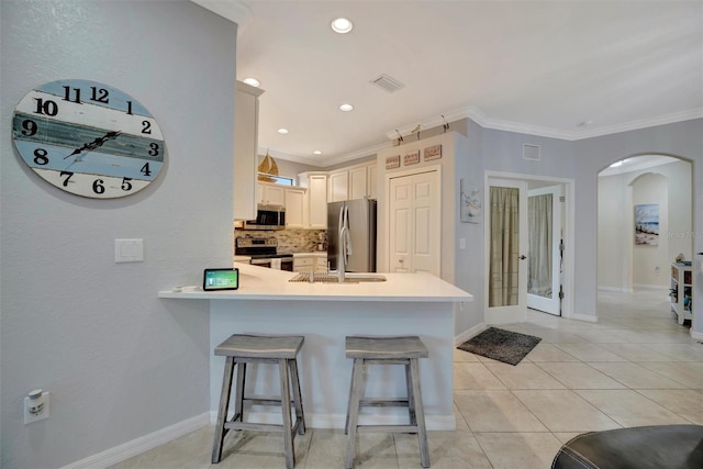 kitchen featuring a peninsula, arched walkways, appliances with stainless steel finishes, crown molding, and a breakfast bar area