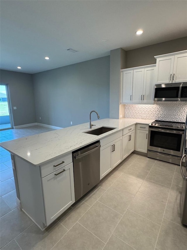 kitchen featuring a peninsula, a sink, tasteful backsplash, appliances with stainless steel finishes, and light tile patterned floors