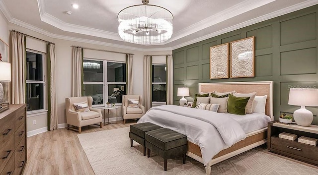 bedroom featuring a tray ceiling, light wood-type flooring, a decorative wall, crown molding, and a notable chandelier