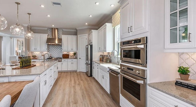 kitchen with a sink, backsplash, white cabinets, wall chimney exhaust hood, and appliances with stainless steel finishes