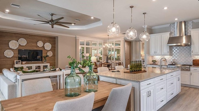 kitchen with wall chimney range hood, open floor plan, crown molding, and ceiling fan with notable chandelier