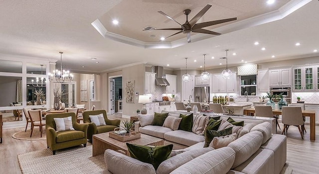 living area featuring ceiling fan with notable chandelier, light wood-style flooring, recessed lighting, and a raised ceiling
