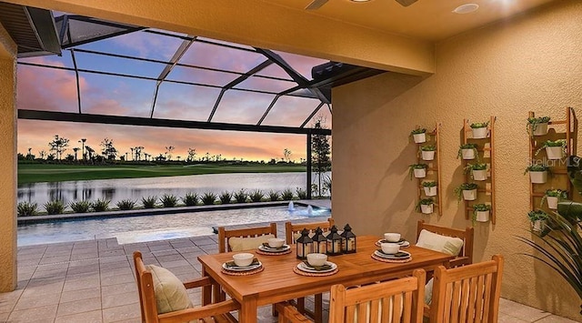 patio terrace at dusk featuring an outdoor pool, a lanai, outdoor dining area, and a water view