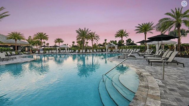 pool at dusk with a gazebo, a community pool, and a patio