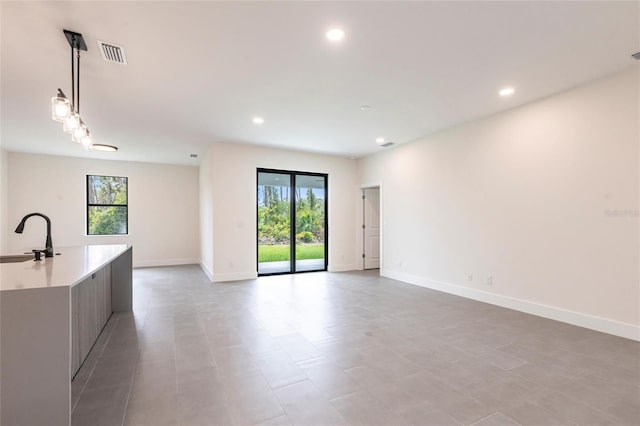 unfurnished living room featuring a sink, healthy amount of natural light, baseboards, and recessed lighting