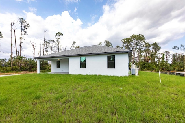 rear view of property with stucco siding, a yard, and roof with shingles