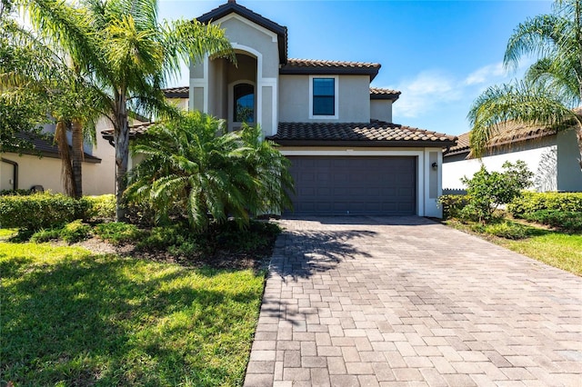 mediterranean / spanish home featuring an attached garage, decorative driveway, stucco siding, and a tiled roof