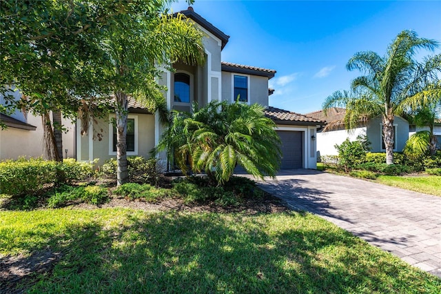 mediterranean / spanish-style home featuring stucco siding, decorative driveway, a garage, a tile roof, and a front lawn