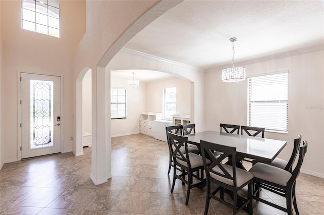 dining space featuring crown molding, arched walkways, a chandelier, and baseboards