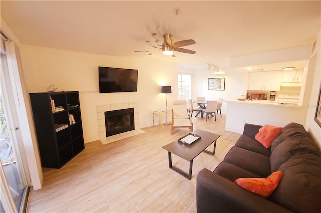 living area with ceiling fan, a tile fireplace, and light wood-type flooring
