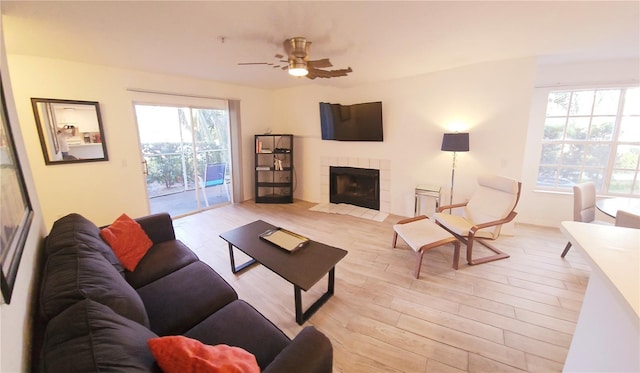 living room with ceiling fan, light wood finished floors, and a tiled fireplace