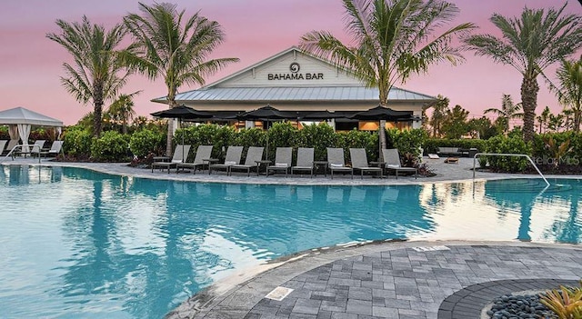 pool at dusk with a patio area, a gazebo, and a community pool