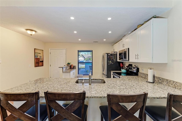 kitchen with a kitchen breakfast bar, light stone countertops, a peninsula, appliances with stainless steel finishes, and white cabinetry