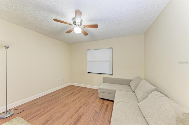 living area with ceiling fan, baseboards, a textured ceiling, and light wood finished floors
