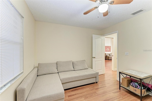 living area featuring light wood-style flooring, visible vents, a textured ceiling, and a ceiling fan