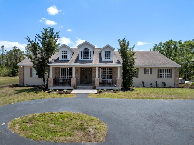 new england style home featuring cooling unit, a porch, a front yard, and a shingled roof