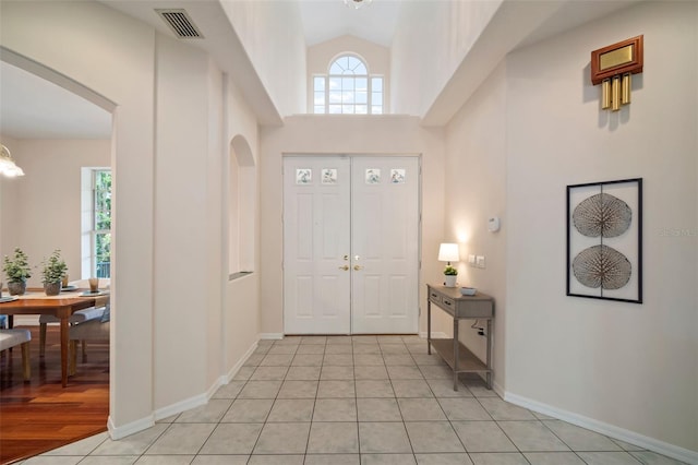 entryway with high vaulted ceiling, a chandelier, light tile patterned floors, arched walkways, and visible vents