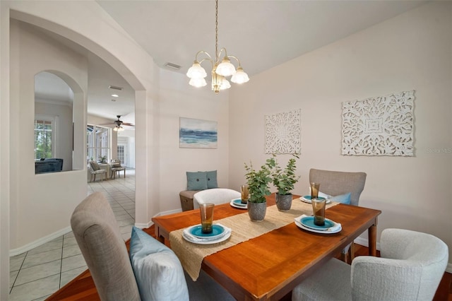 dining area with visible vents, light tile patterned floors, arched walkways, baseboards, and ceiling fan with notable chandelier