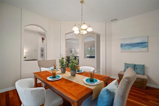 dining space featuring wood finished floors, a chandelier, arched walkways, baseboards, and visible vents