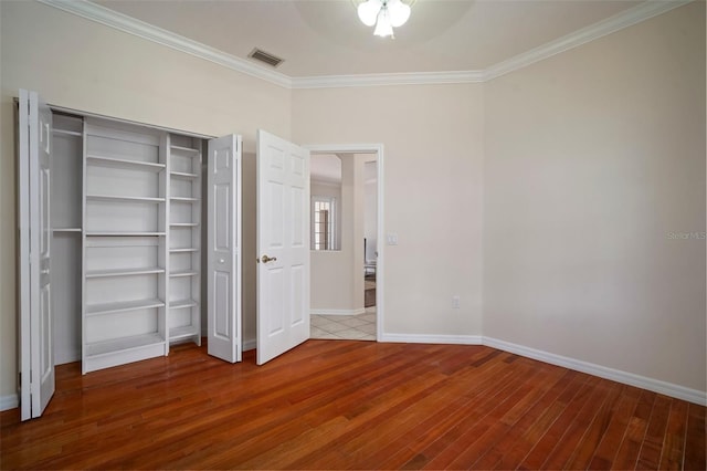 unfurnished bedroom featuring baseboards, crown molding, wood finished floors, and visible vents
