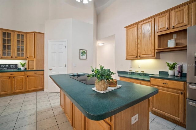 kitchen featuring a high ceiling, dark countertops, light tile patterned flooring, a kitchen island, and glass insert cabinets