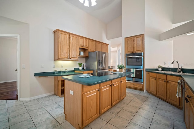 kitchen featuring a towering ceiling, dark countertops, stainless steel appliances, and a kitchen island