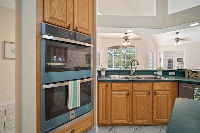 kitchen with dark countertops, a ceiling fan, multiple ovens, and a sink