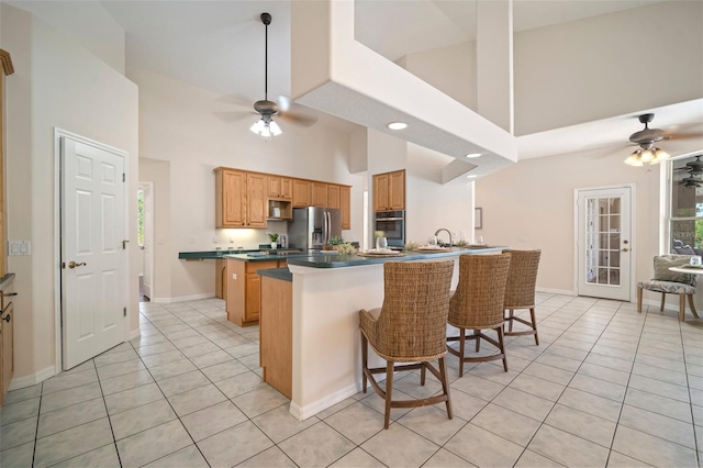 kitchen with stainless steel appliances, a ceiling fan, a towering ceiling, and light tile patterned floors