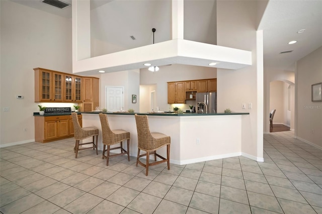 kitchen featuring stainless steel fridge with ice dispenser, dark countertops, arched walkways, light tile patterned flooring, and a kitchen bar