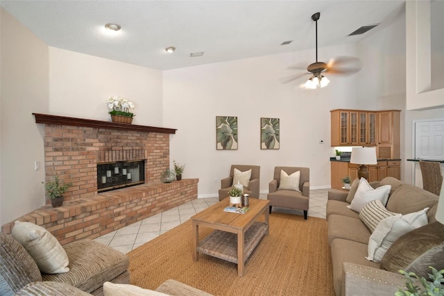 living area with a towering ceiling, a ceiling fan, light tile patterned floors, baseboards, and a brick fireplace
