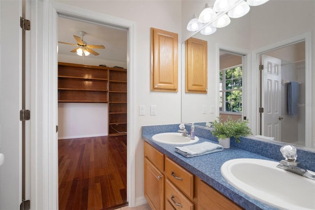 bathroom featuring a ceiling fan, wood finished floors, a sink, and double vanity