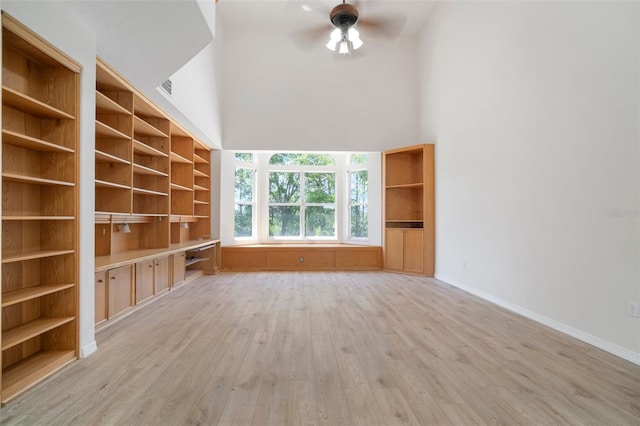 unfurnished living room with a towering ceiling, visible vents, a ceiling fan, light wood-type flooring, and baseboards