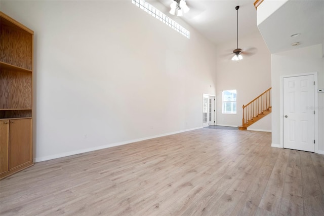 unfurnished living room featuring high vaulted ceiling, ceiling fan, stairs, and light wood finished floors