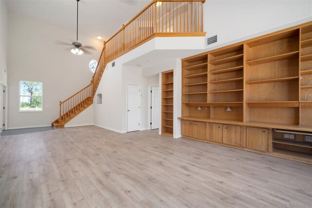 unfurnished living room featuring a ceiling fan, light wood finished floors, baseboards, a high ceiling, and visible vents
