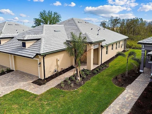 view of side of home featuring a tile roof, driveway, a yard, a garage, and stucco siding