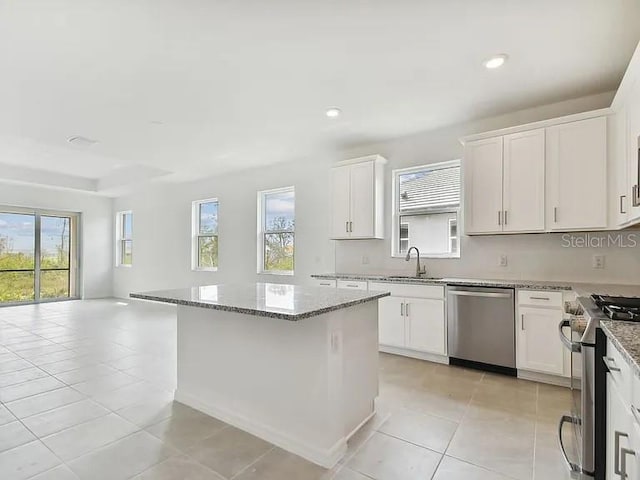 kitchen featuring stainless steel appliances, a sink, open floor plan, light stone countertops, and a kitchen island