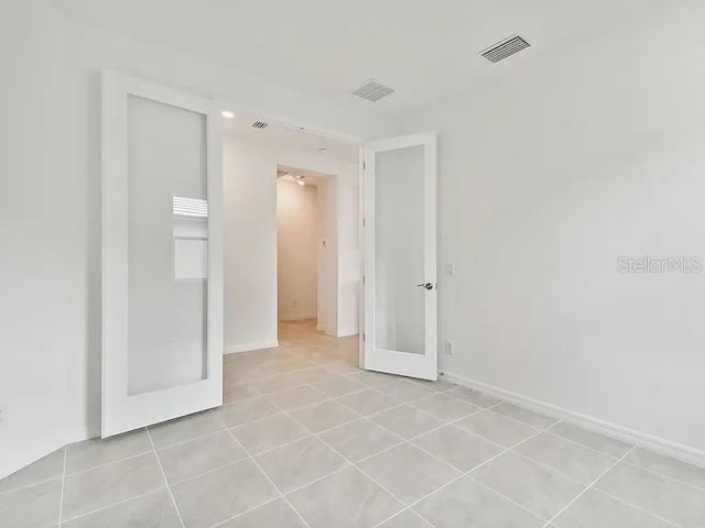 empty room with baseboards, french doors, visible vents, and light tile patterned flooring