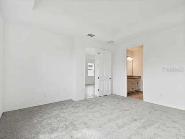unfurnished bedroom with ensuite bath, carpet flooring, visible vents, and baseboards