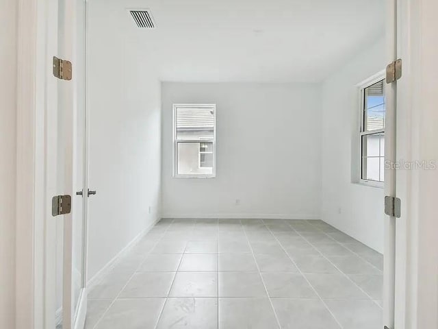 empty room with a wealth of natural light, light tile patterned flooring, and visible vents
