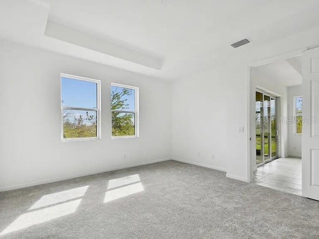 carpeted spare room featuring a raised ceiling, baseboards, visible vents, and plenty of natural light
